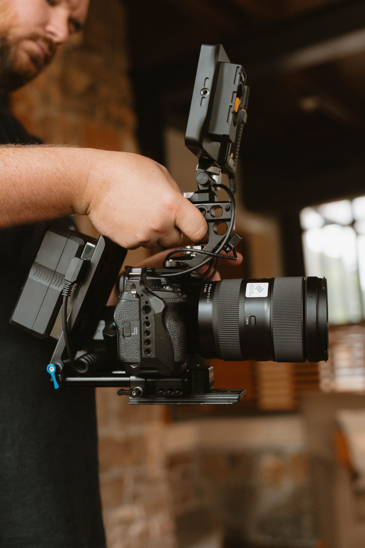 A videographer operating a professional cinema camera rig on location in a warm brick-and-wood setting in Arkansas
