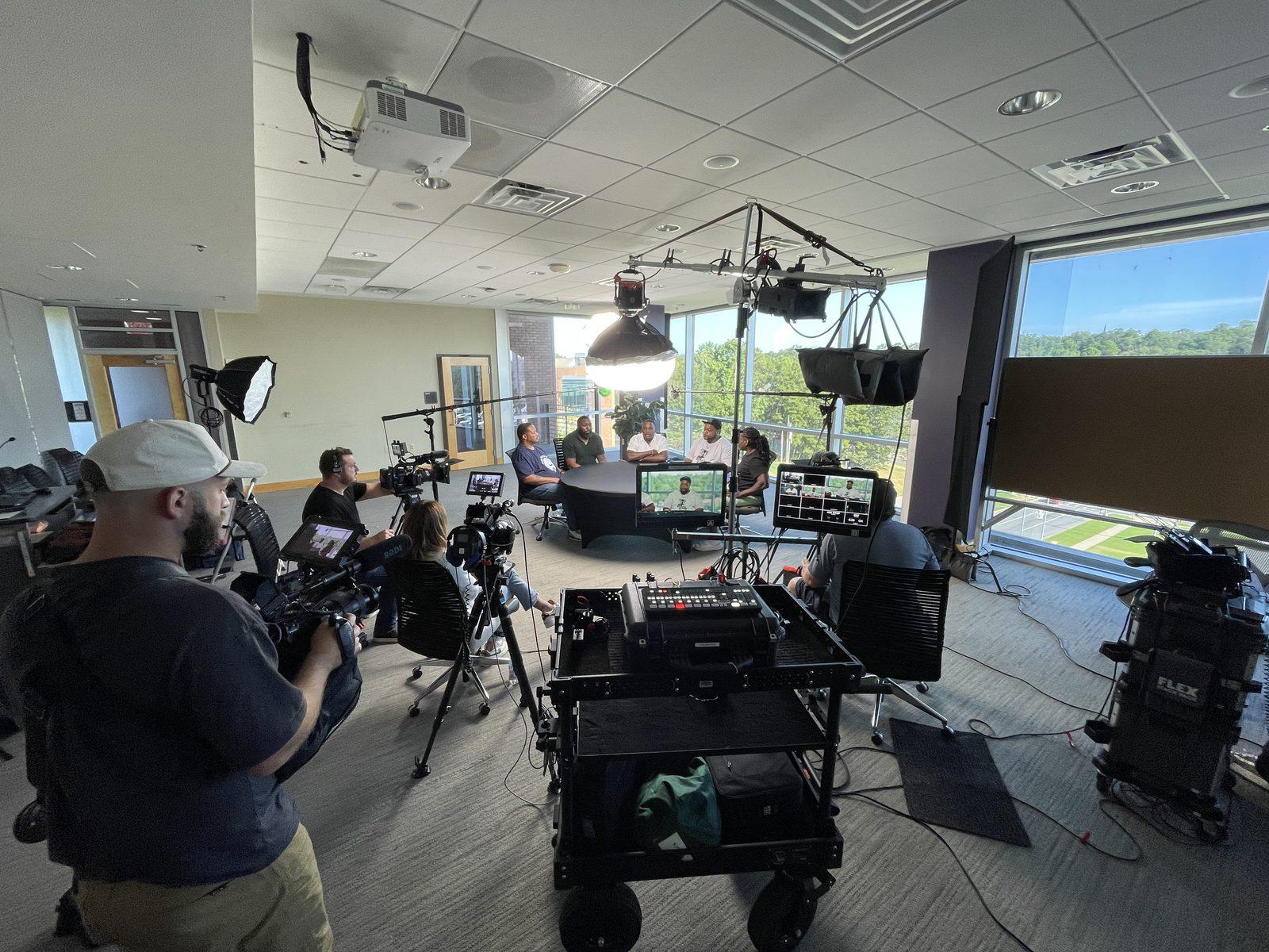 University video production in Arkansas with a multi-person interview setup, professional lighting, and campus view through large windows
