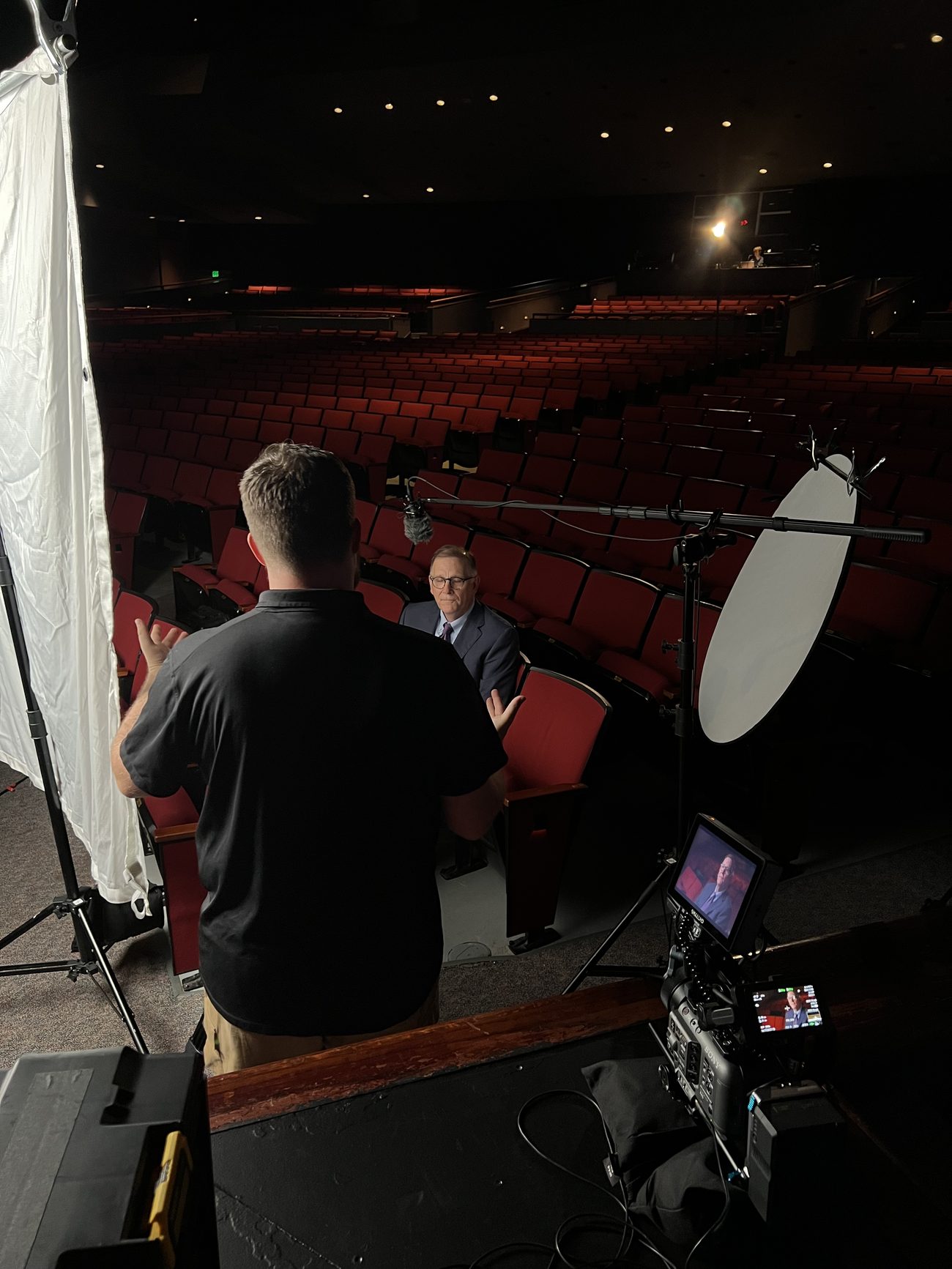 On-camera interview being filmed in a theater in Arkansas, with the director coaching a subject seated in red theater seats